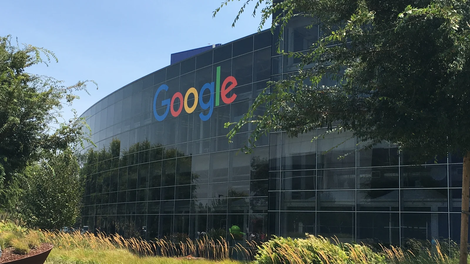 A large curved, glass-fronted office building with the multicolored “Google” logo mounted on its facade.